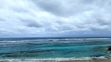 Sakin bir okyanusun manzarası bulutlu bir gökyüzünün altında hafif dalgalar, sakin ve sakin bir atmosfer yaratıyor.