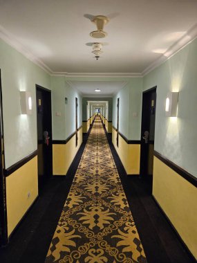 Klasik desenli halı ve yumuşak ışıklandırmalı uzun simetrik otel koridoru.