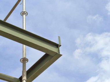 Parlak mavi gökyüzünün altındaki bir inşaat alanında yeşil çelik kiriş iskeleti.