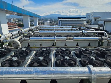 Havalandırma vantilatörlü endüstriyel soğutma üniteleri açık mavi gökyüzünün altındaki yüksek katlı bir çatıya monte edildi. Kentsel sanayi ve inşaat temaları için mükemmel