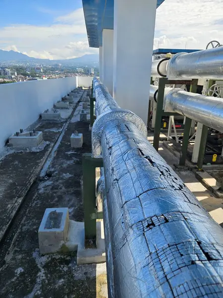 Çatlamış yalıtım malzemesi endüstriyel bir binada, güpegündüz çatıdaki bir boru hattını kaplıyor. Kentsel sanayi ve inşaat temaları için mükemmel