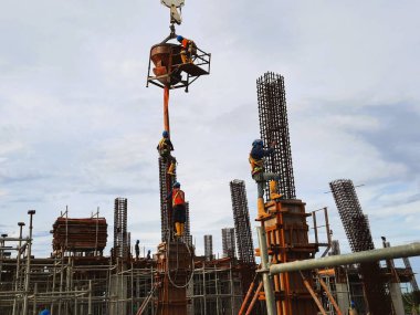 İnşaat işçileri, sanayi, işçilik veya inşaat mühendisliği gibi konular için mükemmel olan yüksek katlı bir projede güçlendirilmiş çelik sütunlara beton döküyorlar.