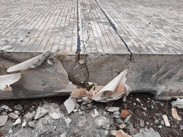 Görünür çatlaklara ve molozlara sahip hasarlı betonun yakın çekimi, inşaat veya altyapı temaları için ideal