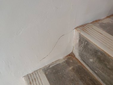 Duvardaki çatlak ve yıpranmış yüzeyi olan merdiven köşesi bina kusurlarını veya bakım sorunlarını göstermek için mükemmel.