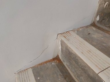 Duvardaki çatlak ve yıpranmış yüzeyi olan merdiven köşesi bina kusurlarını veya bakım sorunlarını göstermek için mükemmel.