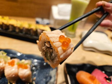 Yemek çubukları ile havada tutulan bir parça suşi, yemek teslimatı için mükemmel pazarlama, yeme anları, ya da yemek tarzı görseller için.