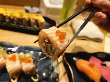 Yemek çubukları ile havada tutulan bir parça suşi, yemek teslimatı için mükemmel pazarlama, yeme anları, ya da yemek tarzı görseller için.