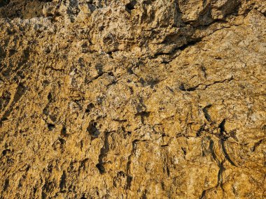 Doğal doku ve çatlakları gösteren sarımsı bir kaya yüzeyinin yakın çekimi, jeolojik temalar, arkaplan tasarımı veya malzeme referansı için idealdir.