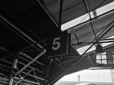 Bir nakliye merkezindeki koyu metal çatı yapısına karşı aydınlatılmış 5 numaralı istasyon levhası yolcuları varış noktalarına yönlendiriyor.