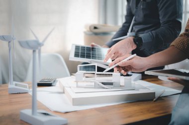 İki mühendis tasarım uzmanı, modelle çalışarak elektrik üretmek ve güneş paneli numunesi üretmek için çatı katında saf enerji kullanımı ve güneş panelleri kurmayı hesaplamayı tartışıyor.