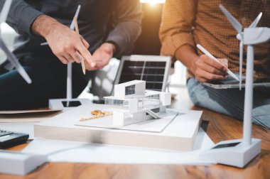 İki mühendis tasarım uzmanı, modelle çalışarak elektrik üretmek ve güneş paneli numunesi üretmek için çatı katında saf enerji kullanımı ve güneş panelleri kurmayı hesaplamayı tartışıyor.
