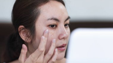 Genç Asyalı kadın cilt bakımını yaparken yanaklarına hafifçe dokunuyor..