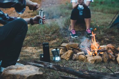 Kamp ateşinde kamp yapan insanlar dağların yakınında kahve demleme ekipmanıyla kamp yapıyorlar..