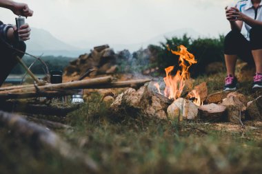 Kamp ateşinde kamp yapan insanlar dağların yakınında kahve demleme ekipmanıyla kamp yapıyorlar. Şenlik ateşine odaklan. * * Odaklan * *