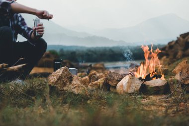 Kamp ateşinde kamp yapan insanlar dağların yakınında kahve demleme ekipmanıyla kamp yapıyorlar..