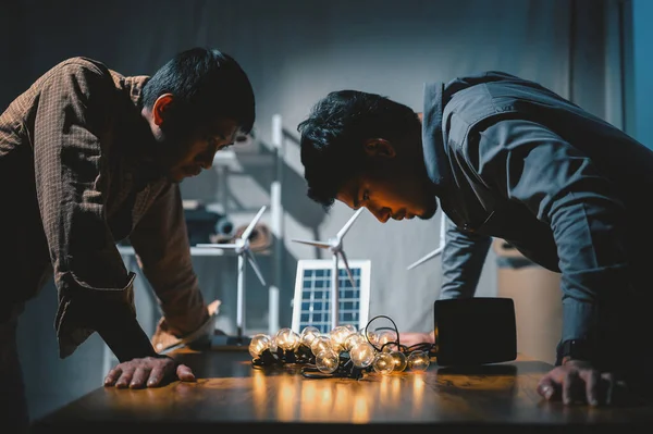 Two Engineers testing efficiency of solar cell panels type with Led light in office at night. Learn design and calculation to energy accumulation, use pure energy nature, solar and wind to output