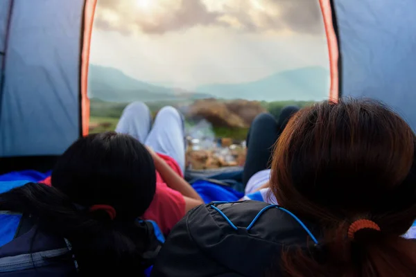 Young women use a trekking bag as a pillow to lie in tents and look up at the sky with views of the natural sunlight on the mountains. Camping with sunset in base camp. **Focus**