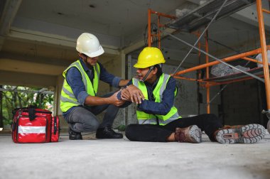 İnşaat alanındaki inşaat işçisinin iş yerinde ilk yardım kazası. Dirsek kazası, Foreman ilk yardım çantası ile çalışan kazasına yardım ediyor..