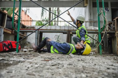 İnşaat alanındaki inşaat işçisinin iş yerinde ilk yardım kazası. İskeleden düşen kaza, Foreman çalışanların ilk yardım çantasıyla kazaya yardım etmesi ve yardım için el sallaması..