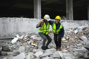 İnşaat ustabaşı inşaat işçilerinin cesetlerini desteklemeye yardım ediyor beton molozların üzerinde ayağa kalkıyor ve ilk yardım odasına gidiyor. Diz kazası.