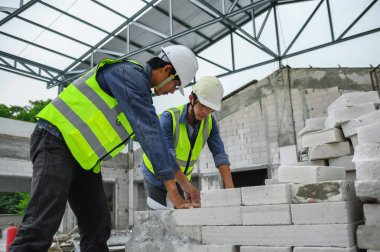 İnşaat mühendisleri ustabaşı veya inşaatçıyla planları açarken ve inşaat alanındaki çelik yapı çatısının altındaki tuğla yığınlarının üzerinde otururken tartıştılar..