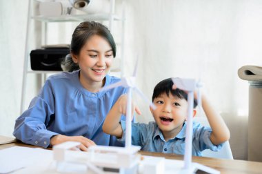 Genç Asyalı anne, enerji mühendisleri oğluna bakmaktan zevk alıyorlar. Küçük oğluyla vakit geçiriyorlar. Ana ofiste rüzgar türbiniyle oynuyorlar..