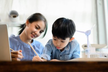 Küçük çocuk annesinin kontrolü altında kalem çizimi ve yazma pratiği yaparken, genç Asyalı anne de küçük oğlu, annesine yardım eden oğlu, Homeschool konseptiyle vakit geçiren bir mimar.