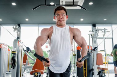 Kaslı bir adam, vücut geliştiren Asyalı bir adam, halat itme egzersizi yapıyor. Triseps kol egzersizleri dengeli üst gövde çekişleri ile spor salonunda kablo makine ağırlık kaldırma, fitness egzersiz konsepti.