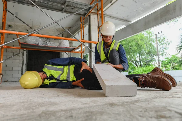 Accident in the construction workplace, concrete block brick falls on an unsuspecting builder\'s leg, Foreman to helping injured colleague or builder in construction site.