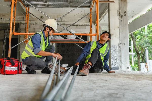 Accident in the construction workplace, Electrical metal conduit pipe falls on an unsuspecting builder\'s leg, Foreman to helping injured colleague or builder with first aid bag in construction site
