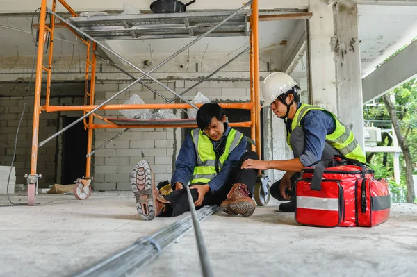 Accident in the construction workplace, Electrical metal conduit pipe falls on an unsuspecting builder's leg, Foreman to helping injured colleague or builder with first aid bag in construction site