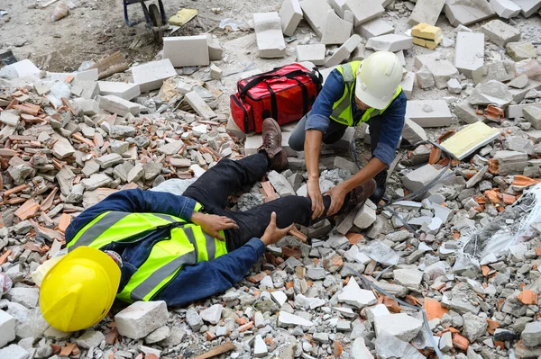 First aid support accident at work of builder worker on the concrete cement rubble in construction site. Knee accident and ankle pain in work, Foreman help employee accident with first aid bag.