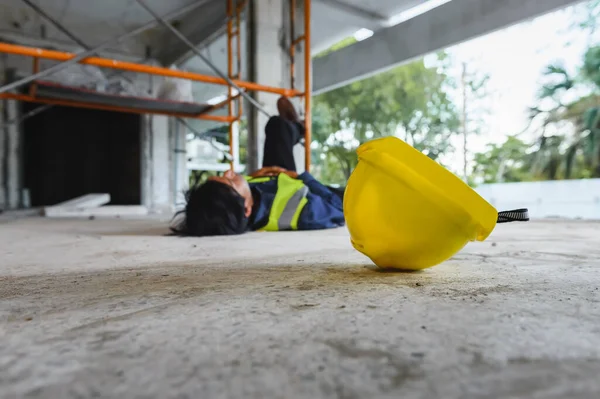 Yellow hard hat from construction worker accident falls from scaffolding in background,  Work accidents in the workplace at construction site area, lying unconscious on floor, Unsafe concept