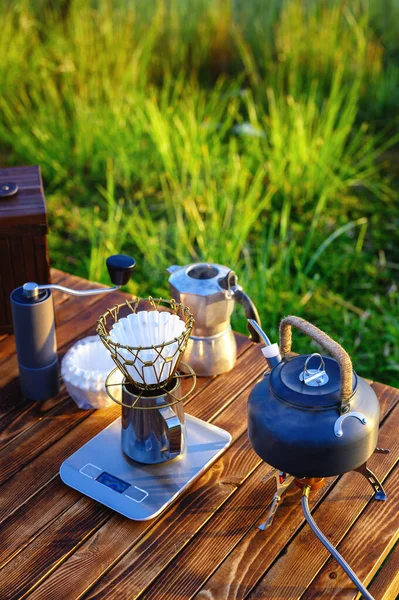 Outdoor coffee drink on wooden table with natural mountain background and soft sunrise, coffee drip with other equipment. Vertical image with copy space.