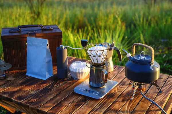 Outdoor coffee drink on wooden table with natural mountain background and soft sunrise, coffee drip with other equipment.