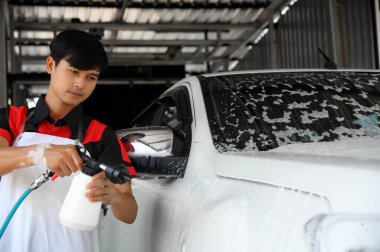 Erkek İşçi, araba yıkama ve bakımında kullanılan köpük spreyini özenle yıkama, araba yıkama ve araba yıkama ile otomotiv bakımı için parlak ve temiz araçları detaylandırmada kullanır..