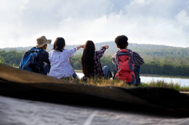 Asyalı genç insan grupları oturur ve dağ gölü manzaralarına bakar ve doğal parktaki kamp çadırlarının yanında dinlenirler. Özgürlüğün tadını çıkarmak ve yaz mevsiminde dostluk konseptiyle rahatlamak.