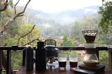 Açık hava kahve makineleri masa ahşap terasına kurulmuş ve sabah doğal dağ arka planına sahip kahve damlaları ve fotokopi alanı olan diğer ekipmanlarla dolu..