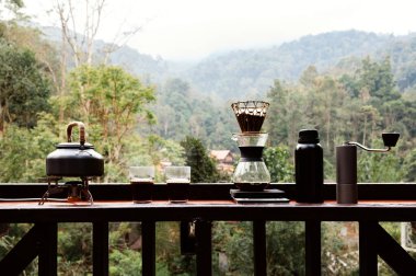 Açık hava kahve makineleri masa ahşap terasına kurulmuş ve sabah doğal dağ arka planına sahip kahve damlaları ve fotokopi alanı olan diğer ekipmanlarla dolu..