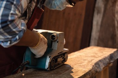 Zımparalama makinesi zımpara makinesi kullanarak yüzey tahtasını düzleştiriyorum. Marangoz marangozluk atölyesinde el yapımı elektrikli zımpara makinesi kullanır. Makinede hareket hissi için yakın çekim ve seçici yumuşak odak