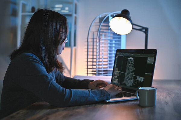 Asian architect or women engineer use laptop study detail and construction design alone in drawing in an office room at night with building model on desks office.