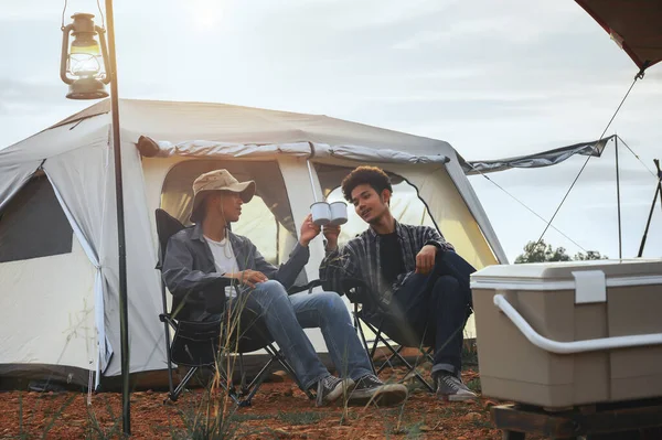 Asian young man two persons sitting enjoy coffee drink near a camping tent in the morning time, coffee drink relaxing on the morning summer camping vacation.