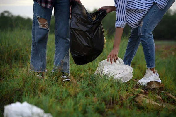 Closeup of hands with plastic garbage bags. Two female volunteers collect garbage and plastic waste bag into garbage bags at nature park. Awareness of pollution to nature, Environmental conservation.