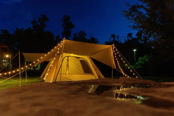 Outdoor camping tent with tarp or flysheet on grass courtyard and warm night light under dark blue sky twilight time, family vacation picnic on holiday relax, Overview of camping of family tourist.  **Focus**