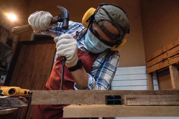 Carpenter hand with chisel in hand working on carpentry. Carpenter wearing safety equipment while chiseling and making wooden products in a home workshop.