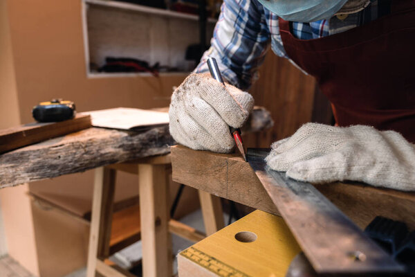 Close up hand of carpenter using square angle ruler tool and pencil to mark position on wood for cut in the carpentry workshop.
