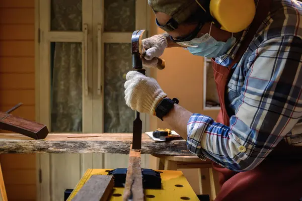 Carpenter hand with chisel in hand working on carpentry. Carpenter use chisel making to wooden products in a home workshop. Selection focuses on hand while chiseling.
