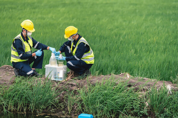 Два инженера-эколога берут пробы воды у природных источников возле фермы, возможно, загрязненные токсичными отходами или подозрительным загрязнением мест с копировальным пространством.