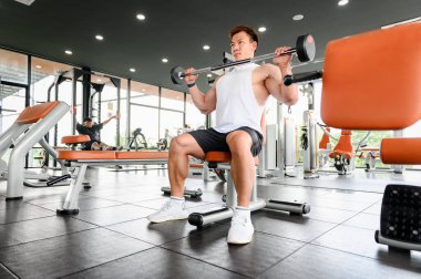 Jimnastik salonunda ağırlık kaldıran kaslı vücut geliştirici Asyalı adam ağırlık kaldırma egzersizleriyle kol kaslarını çalıştırıyor. Fitness kas geliştirme konseptini çalıştırır.