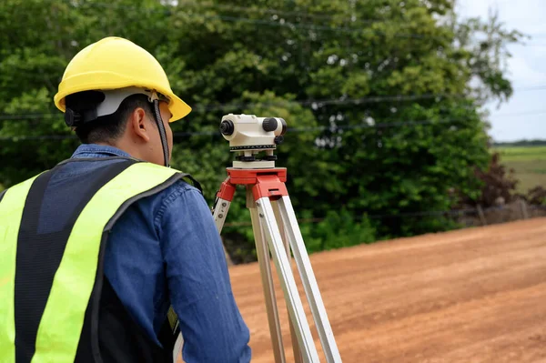 Asian surveyor engineer checking level of soil with Surveyor\'s Telescope equipment to measure leveling for cut and fill, started leveling the ground at the highway road construction site.